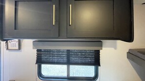 A kitchen with two dark cabinets, a window with blinds, and a sign that says "ENJOY LIFE". - Welcome to Cozy by the Coast! Just steps from the beach, ocean is calling you! (Surfside Beach)