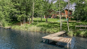 Una cabaña rodeada de bosque, un muelle que se adentra en un lago y una zona verde con un columpio.