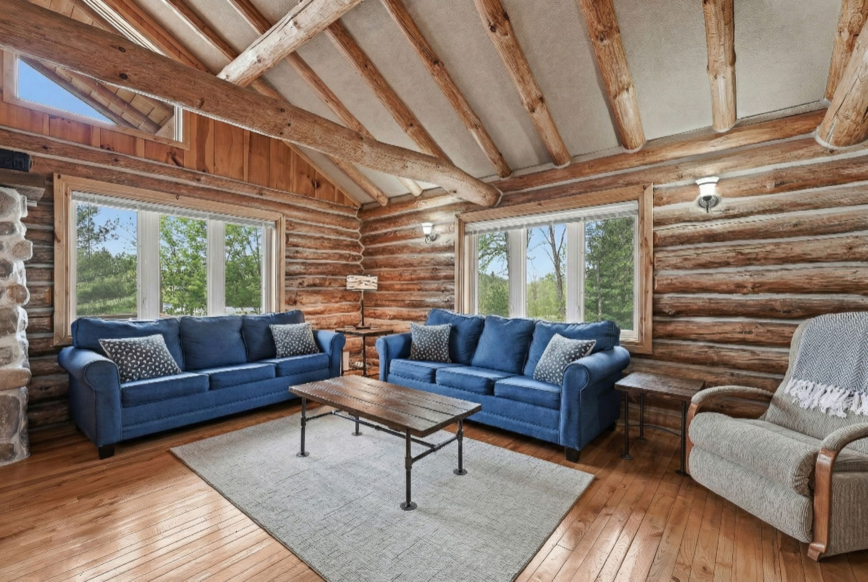 A log cabin interior with two blue sofas, a wooden coffee table, and a stone fireplace.