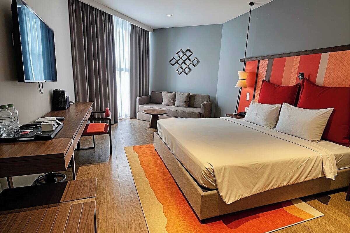 Ein Hotelzimmer mit einem Bett, einem Schreibtisch, einer Couch, einem Fernseher und einer Wandleuchte.