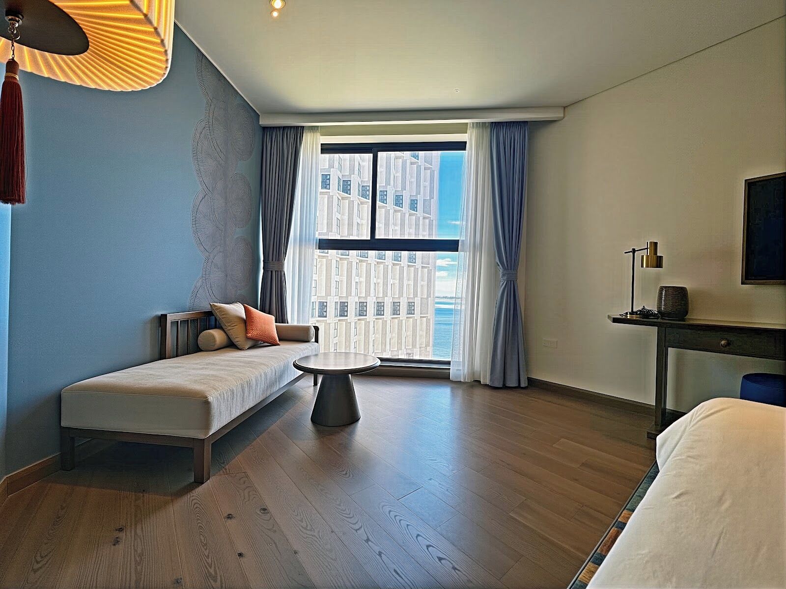 A modern hotel room with a sofa, a small table, a bed, a TV, and a balcony with a city view.