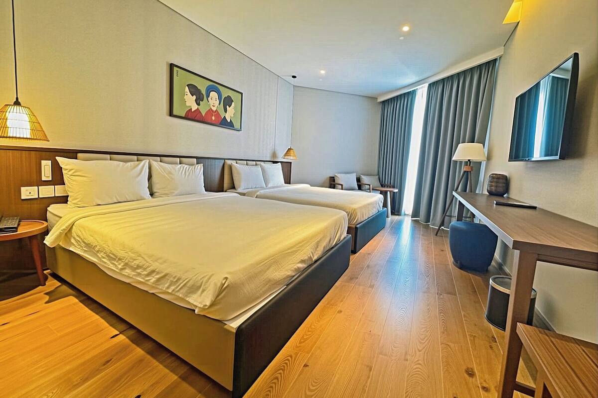 Ein Hotelzimmer mit zwei Betten, einem Schreibtisch, einem Sessel, einem Fernseher und einem Bild an der Wand.