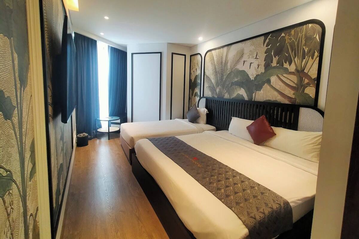 Ein Hotelzimmer mit zwei Betten, einem kleinen Tisch, einem Sessel, einem großen Fenster mit Vorhängen und einer Wand mit einem Wandbild zum Thema Natur.