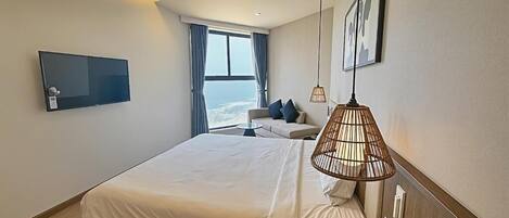 A modern hotel room with a large bed, a sofa, a television, and a view of the sea.