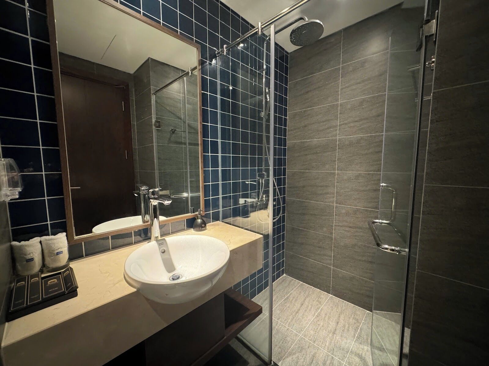 Un baño moderno con cabina de ducha de vidrio, un espejo grande y encimera color crema.