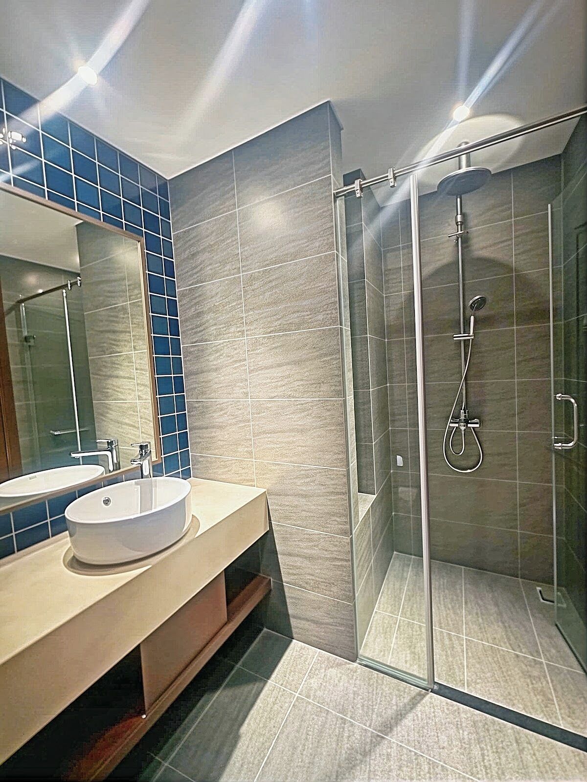 Un baño moderno con ducha de vidrio, un espejo grande y un tocador beige con lavamanos.