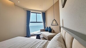 Una camera d'albergo con un letto, un divano, un tavolino e vista sull'oceano.