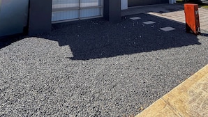 Um edifício residencial com garagem, entrada para carros e estacionamento de cascalho.