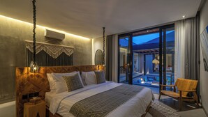A modern bedroom with a large bed, a wooden headboard, a nightstand, and a view of a balcony. - Kiena Ubud (Ubud)