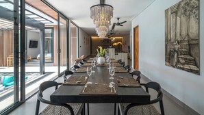 A modern dining area with a long table set for a meal, a chandelier, and a large painting on the wall. - Kiena Ubud (Ubud)