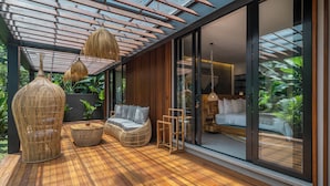 A modern outdoor living area with a wooden deck, wicker furniture, and a glass door leading to a bedroom. - Kiena Ubud (Ubud)