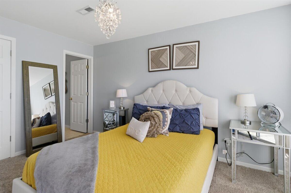 A bedroom with a bed, bedside tables, a mirror, and a chandelier.