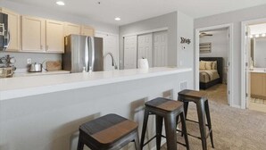 A modern kitchen with white cabinets, a stainless steel refrigerator, and a bar area with stools.