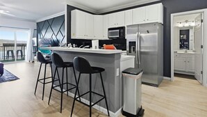 Een moderne keuken met witte kasten, een roestvrijstalen koelkast en een bar met krukken.