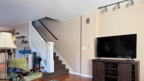 A living room with a TV, wooden furniture, a staircase, and a lamp. - Charming 2 BR Whole-house rental Explore Historic Bethlehem (Bethlehem)