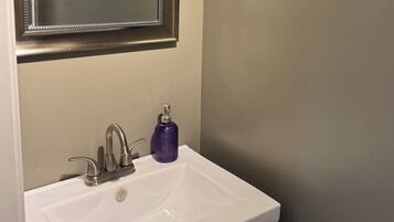 Ein Waschbecken mit Spiegel darüber, einem Wasserhahn und einem violetten Seifenspender.