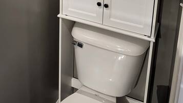 A toilet with a white tank and lid, a chrome flush handle, and a white cabinet above it.
