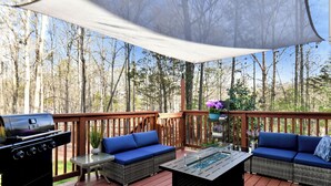 Una terrazza con barbecue, sedute imbottite blu, un tavolo in vetro e vista sugli alberi.