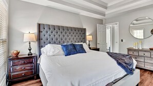 Una camera da letto con una testiera trapuntata, un letto con biancheria bianca, due comodini con lampade, una cassettiera e una ventola a soffitto.