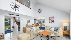 Un salón amplio con un sofá seccional beige grande, una mesa de centro redonda y una zona de comedor con sillas de madera.