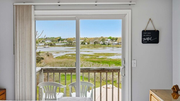 Una habitación con un amplio ventanal corredero que da a un balcón con vistas a una zona residencial y una masa de agua.