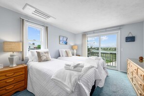 A bedroom with two beds, a dresser, a lamp, and a view of the outdoors. - Waterfront Escape with Stunning Views on Bass River (West Dennis)
