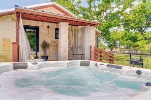 A hot tub area with stone walls and a wooden pergola, surrounded by a fenced yard and trees. - Elm Cottage - Hot Tub & 1 mile from Main st (Fredericksburg)