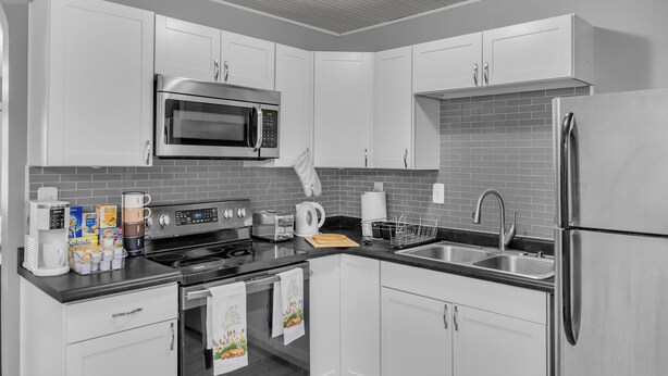 Una cucina moderna con mobili bianchi, frigorifero in acciaio inox, forno a microonde, piano cottura e lavello.
