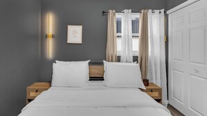 Una camera da letto con un letto, due comodini, una lampada a parete, un quadro incorniciato e una finestra con tende.
