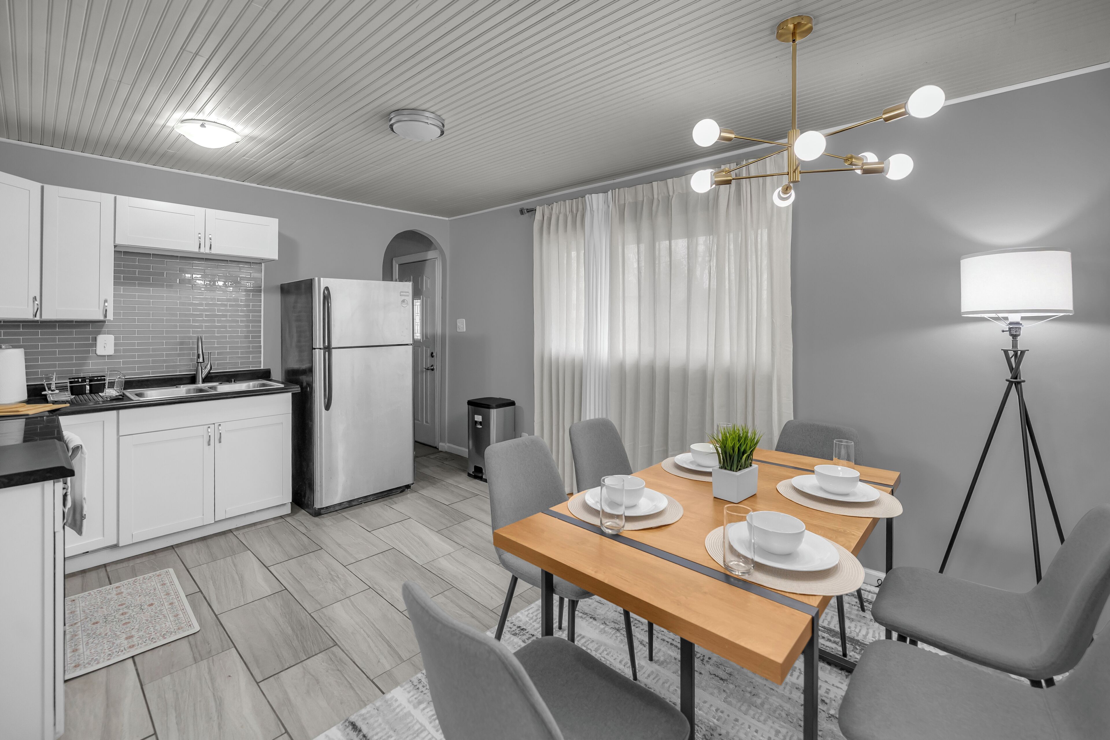 A modern kitchen with white cabinets, a stainless steel refrigerator, and a dining area with a wooden table set for four.