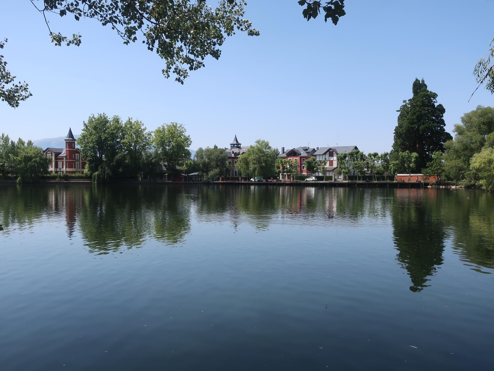 A calm lake with buildings in the background, including a red building with a tower.