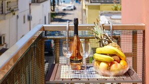 Een balkon met een fles wijn, twee glazen en een schaal fruit.