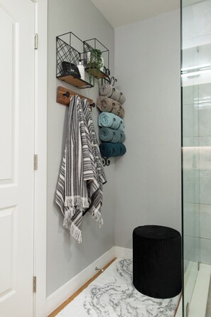 Une salle de bain avec une porte blanche, un tabouret noir, un tapis à motifs de marbre et des serviettes rangées sur un porte-serviettes.