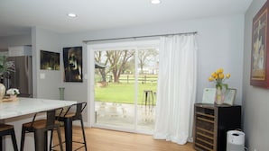A modern kitchen with a large sliding glass door leading to a backyard. There are two bar stools, a refrigerator, and a small table with a vase of flowers. - 3-bedroom house in pleasant Paso Robles with cool vibes (Paso Robles)