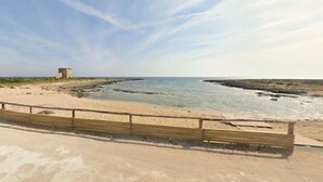 En strand med et træværn, en lille bygning og rolige bølger.