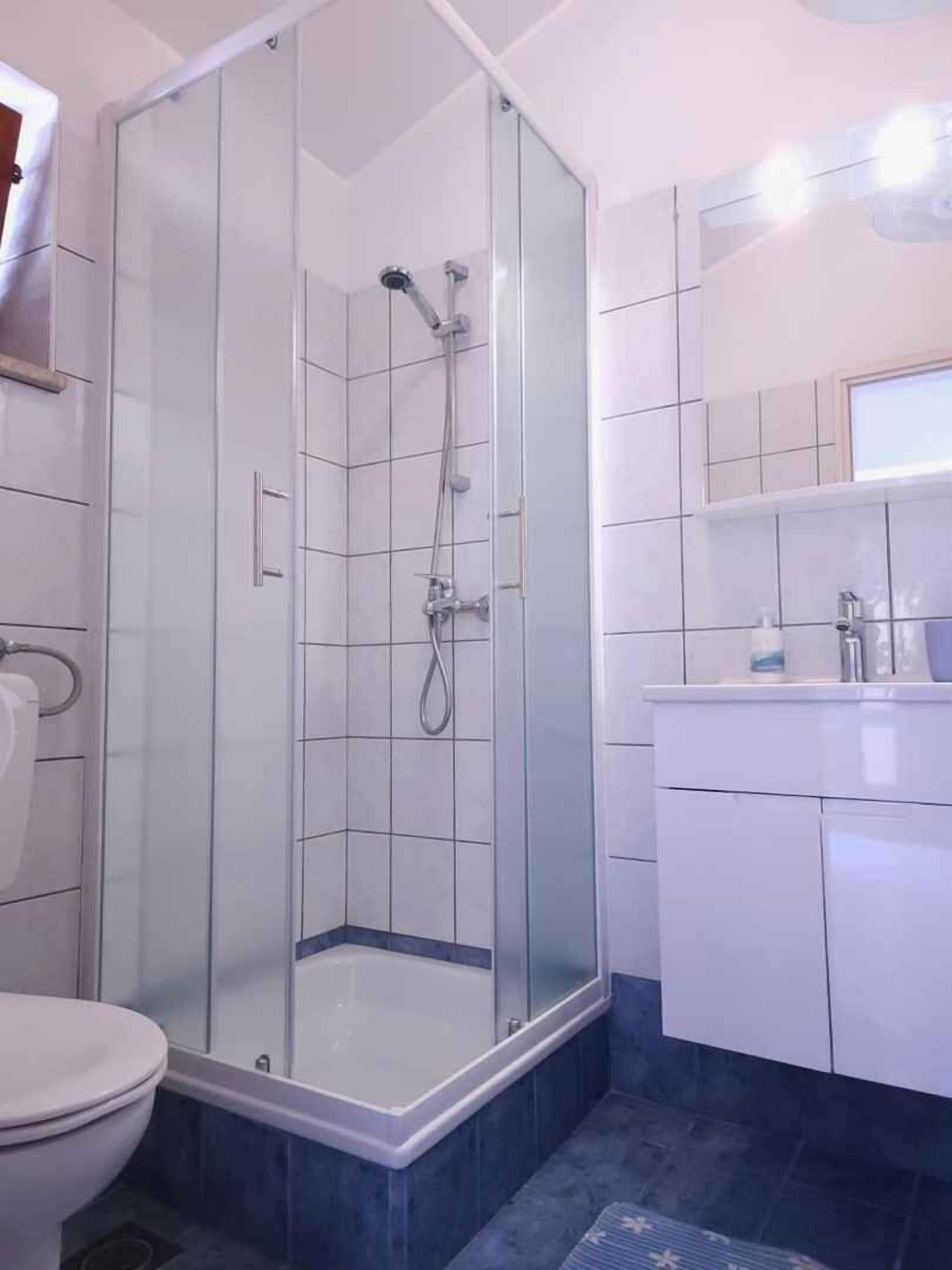 Kylpyhuoneessa on lasiseinällä varustettu suihku, wc ja pesuallas, jonka yläpuolella on peili.
