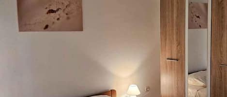 A bedroom with a bed, a nightstand, a lamp, and a wardrobe.