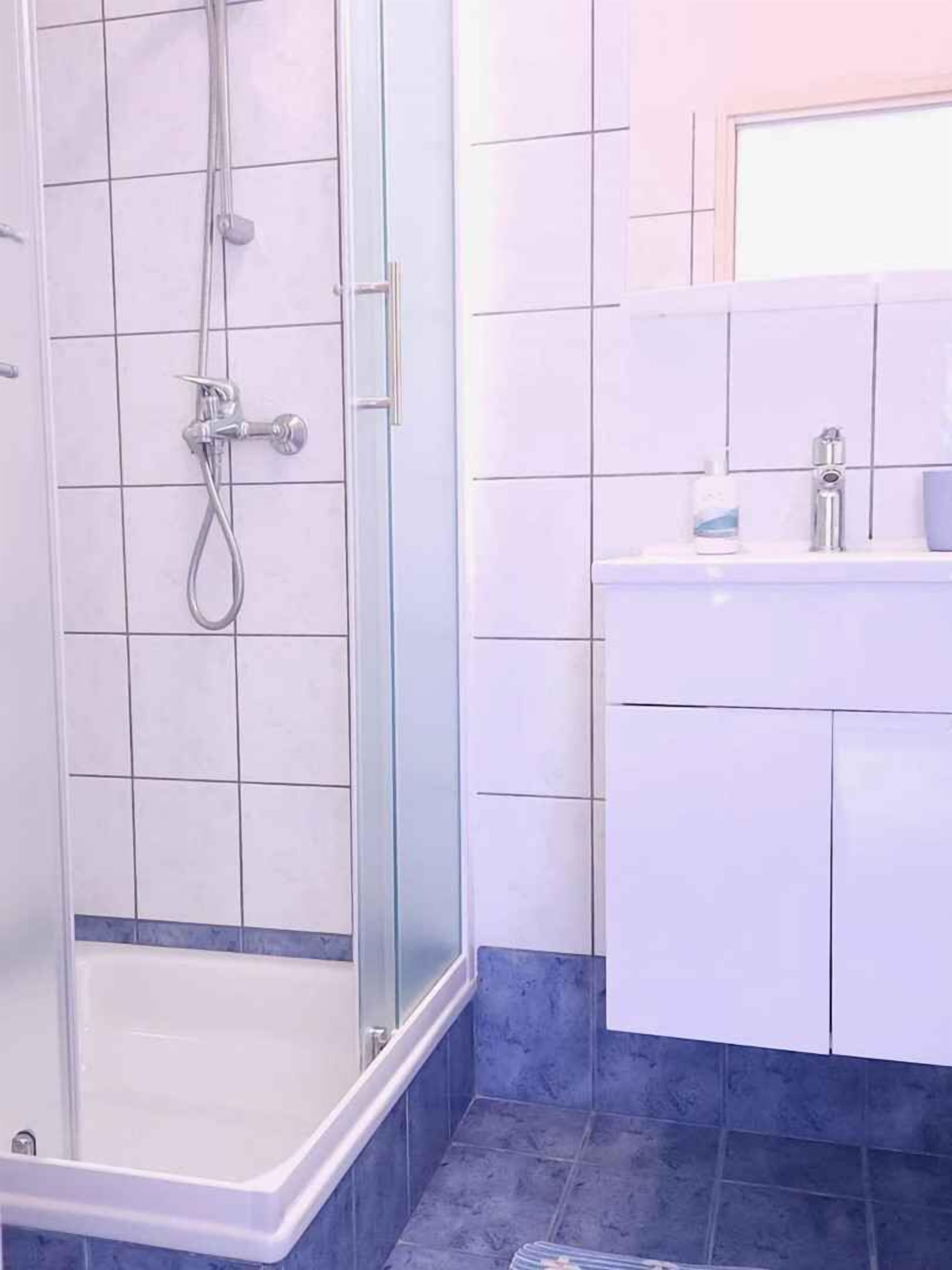 A bathroom with a glass-enclosed shower, a white sink, and blue-tiled flooring.