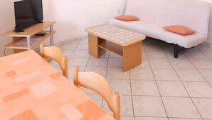 A small, well-lit room with a white sofa, a wooden table with chairs, a TV on a small stand, and a framed picture on the wall. - Holiday apartment mit Klimaanlage (Pula)