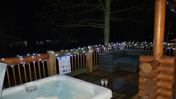 A hot tub, wooden deck, and seating area with string lights. - Bumblebee Log Cabin Felmoor Park (Northumberland)