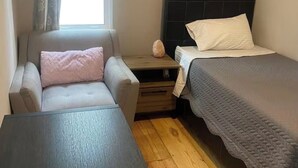 Un dormitorio pequeño y ordenado con una cama individual, una silla y una mesita.