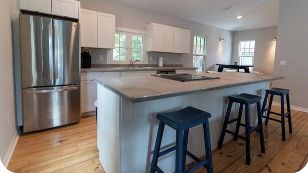 Una cocina moderna con armarios blancos, un refrigerador de acero inoxidable, una isla central con taburetes y suelo de madera.