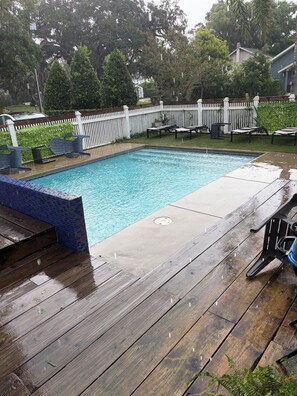 Piscina retangular com borda revestida em azulejo, rodeada por um deck de madeira.