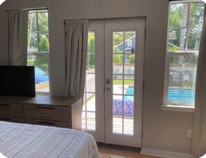 Un dormitorio con cama, cómoda, televisor y puerta corrediza de vidrio que da a una zona de piscina.