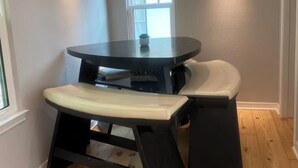 Un pequeño comedor con una mesa redonda y un banco, una ventana y una lámpara en la pared.