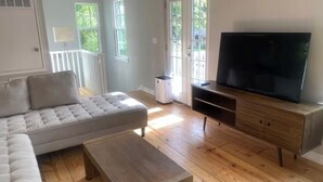 Una sala de estar con sofá, mesa de centro, mueble para la televisión y piso de madera.