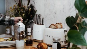 A kitchen counter with a coffee maker, toaster, croissants, and a jar of jam.