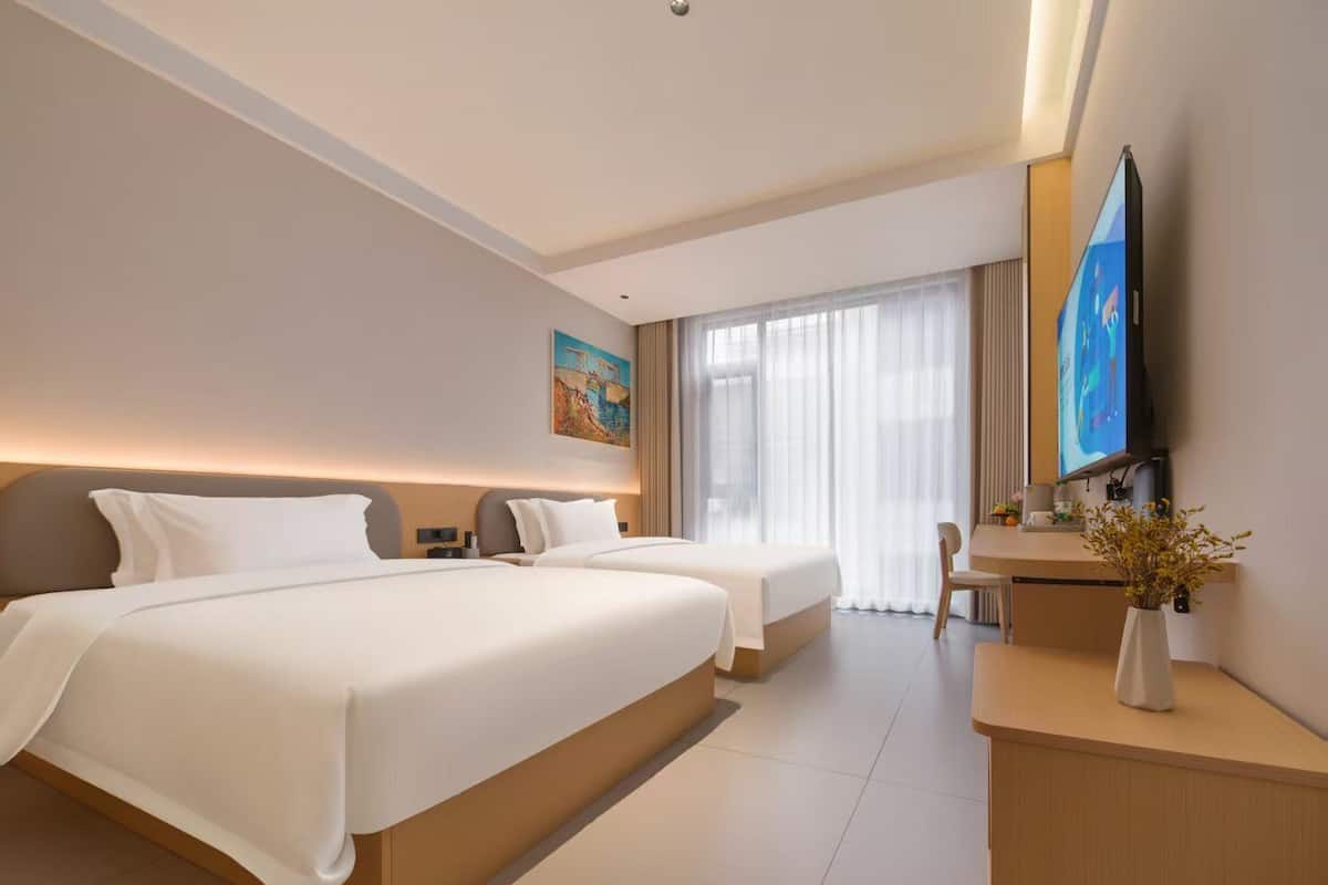 A modern hotel room with two beds, a desk, a TV, and a painting on the wall.