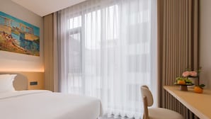 A hotel room with a large bed, a desk with a chair, a painting on the wall, and sheer curtains. - Yixinju Holiday Homestay (Zhangjiajie)