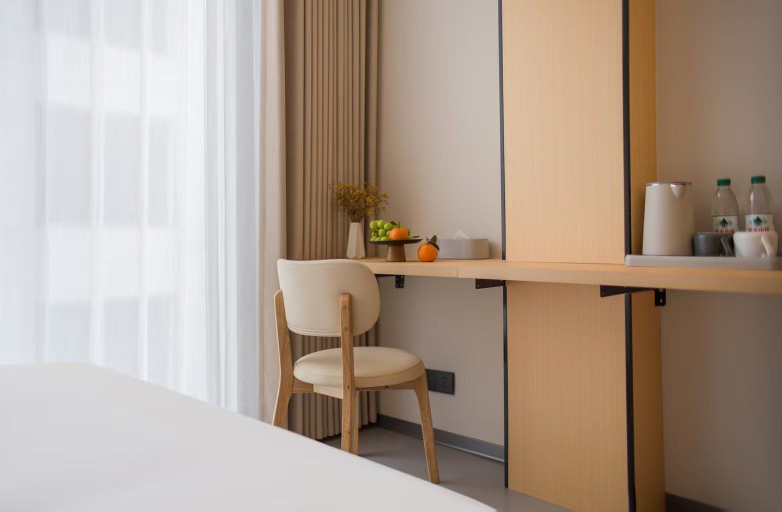 A modern hotel room with a wooden desk, a chair, a small plant, and a vase with flowers.
